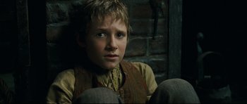 Movie still from “Oliver Twist” (2005), directed by Roman Polanski – A young boy sitting on the ground in front of a brick wall; Close Up shot, High angle