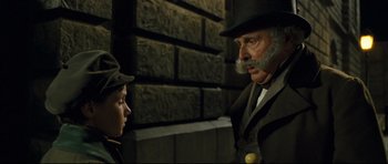 Movie still from “Oliver Twist” (2005), directed by Roman Polanski – A man and a boy in a suit and top hat talking to each other; Close Up shot, Over the shoulder angle