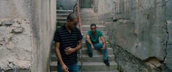 Movie still from “Omar” (2013), directed by Hany Abu-Assad – Two young men sitting on some steps in a building; Wide shot, High angle