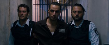 Movie still from “Omar” (2013), directed by Hany Abu-Assad – A group of men standing next to each other in a jail cell; Medium shot, Over the shoulder angle