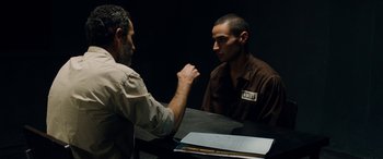 Movie still from “Omar” (2013), directed by Hany Abu-Assad – Two men are sitting at a table and one is holding his fist up; Medium shot, Over the shoulder angle