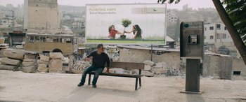 Movie still from “Omar” (2013), directed by Hany Abu-Assad – A man sitting on top of a wooden park bench; Extreme Wide shot, Low angle