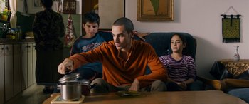 Movie still from “Omar” (2013), directed by Hany Abu-Assad – A man sitting on a couch next to two other people; Medium shot, Over the shoulder angle