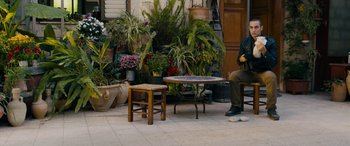 Movie still from “Omar” (2013), directed by Hany Abu-Assad – A man sitting at a table in front of many potted plants; Wide shot, High angle