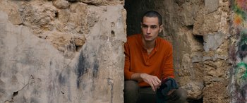 Movie still from “Omar” (2013), directed by Hany Abu-Assad – A man in an orange shirt leaning against a wall; Medium shot, Over the shoulder angle