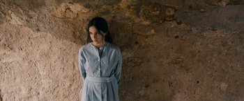 Movie still from “Omar” (2013), directed by Hany Abu-Assad – A woman in a blue striped dress standing in front of a rock wall; Medium shot, Over the shoulder angle