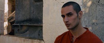 Movie still from “Omar” (2013), directed by Hany Abu-Assad – A man in an orange shirt standing in front of a wall; Close Up shot, Low angle