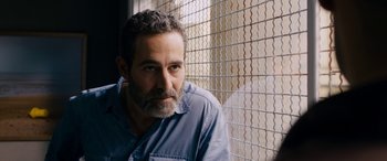 Movie still from “Omar” (2013), directed by Hany Abu-Assad – A man with a goatee is sitting in front of a chain link fence; Close Up shot, Over the shoulder angle