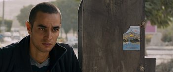 Movie still from “Omar” (2013), directed by Hany Abu-Assad – A young man standing next to a wooden board; Close Up shot, Over the shoulder angle