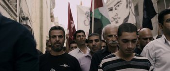 Movie still from “Omar” (2013), directed by Hany Abu-Assad – A group of men standing next to each other holding flags; Medium shot, High angle