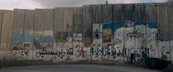 Movie still from “Omar” (2013), directed by Hany Abu-Assad – A man standing on the side of a wall with graffiti on it; Extreme Wide shot, Low angle