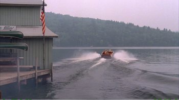 Movie still from “On Golden Pond” (1981), directed by Mark Rydell – A motorboat speeds across a body of water near a dock; Extreme Wide shot, High angle