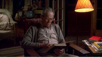 Movie still from “On Golden Pond” (1981), directed by Mark Rydell – An older man sitting in a chair reading a book; Medium shot, High angle
