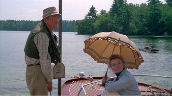 Movie still from “On Golden Pond” (1981), directed by Mark Rydell – A man and a woman standing on a boat in the water holding an umbrella; Medium shot, High angle
