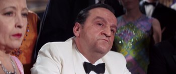 Movie still from “On Her Majesty's Secret Service” (1969), directed by Peter R. Hunt – An older man in a white suit with a bow tie; Close Up shot, Low angle