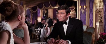 Movie still from “On Her Majesty's Secret Service” (1969), directed by Peter R. Hunt – A man in a tuxedo sitting in front of a table; Medium shot, Over the shoulder angle