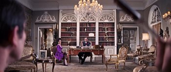 Movie still from “On Her Majesty's Secret Service” (1969), directed by Peter R. Hunt – A man and a woman sitting at a desk in front of a book case; Wide shot, Low angle