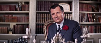 Movie still from “On Her Majesty's Secret Service” (1969), directed by Peter R. Hunt – A man in a suit sitting in front of a book shelf; Close Up shot, Low angle