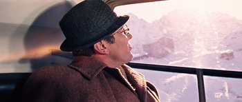 Movie still from “On Her Majesty's Secret Service” (1969), directed by Peter R. Hunt – A man wearing a hat looking out the window of an airplane; Close Up shot, Over the shoulder angle