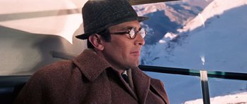 Movie still from “On Her Majesty's Secret Service” (1969), directed by Peter R. Hunt – A man in a hat and glasses looking out a window; Close Up shot, Low angle