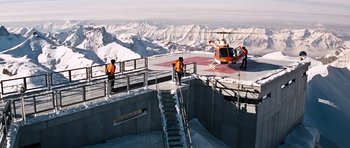 Movie still from “On Her Majesty's Secret Service” (1969), directed by Peter R. Hunt – A group of people standing on a ramp near a helicopter; Extreme Wide shot, High angle