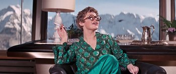 Movie still from “On Her Majesty's Secret Service” (1969), directed by Peter R. Hunt – A woman sitting on a chair holding a cigarette; Medium shot, Low angle