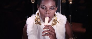 Movie still from “On Her Majesty's Secret Service” (1969), directed by Peter R. Hunt – A woman in a white fur vest is eating a banana; Close Up shot, Low angle