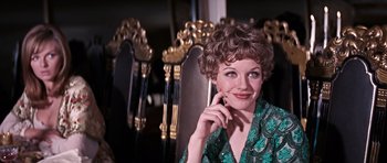Movie still from “On Her Majesty's Secret Service” (1969), directed by Peter R. Hunt – A woman sitting in front of a row of golden chairs; Close Up shot, Over the shoulder angle