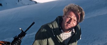 Movie still from “On Her Majesty's Secret Service” (1969), directed by Peter R. Hunt – A man with curly blonde hair wearing a green jacket; Close Up shot, Low angle