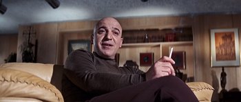 Movie still from “On Her Majesty's Secret Service” (1969), directed by Peter R. Hunt – A man sitting on a couch holding a cell phone; Medium shot, Low angle