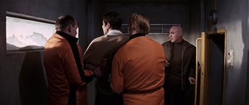 Movie still from “On Her Majesty's Secret Service” (1969), directed by Peter R. Hunt – A group of men standing next to each other in a room; Medium shot, Over the shoulder angle