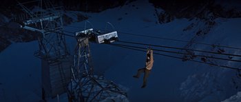 Movie still from “On Her Majesty's Secret Service” (1969), directed by Peter R. Hunt – A man hanging from a ski lift while holding a ski pole; Wide shot, Overhead angle