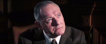 Movie still from “On Her Majesty's Secret Service” (1969), directed by Peter R. Hunt – An older man in a suit and tie looking to his left; Close Up shot, Low angle