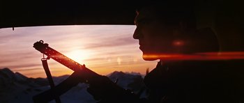 Movie still from “On Her Majesty's Secret Service” (1969), directed by Peter R. Hunt – A man holding a cell phone in front of a sunset; Close Up shot, Low angle