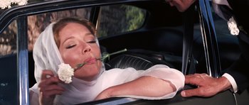 Movie still from “On Her Majesty's Secret Service” (1969), directed by Peter R. Hunt – A woman in a car with a flower in her mouth; Close Up shot, Low angle
