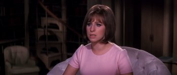 Movie still from “On a Clear Day You Can See Forever” (1970), directed by Vincente Minnelli – A woman in a pink shirt sitting in front of a book case; Close Up shot, Over the shoulder angle