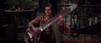 Movie still from “On a Clear Day You Can See Forever” (1970), directed by Vincente Minnelli – A man sitting down holding a guitar in his hands; Medium shot, Low angle