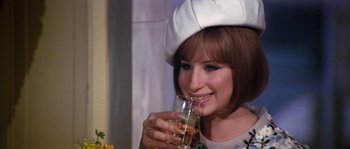 Movie still from “On a Clear Day You Can See Forever” (1970), directed by Vincente Minnelli – A woman wearing a white hat drinking a glass of water; Close Up shot, High angle