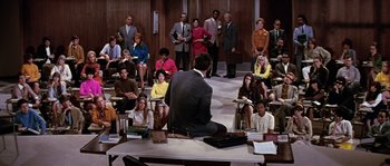 Movie still from “On a Clear Day You Can See Forever” (1970), directed by Vincente Minnelli – A group of people sitting in a room with a man in a suit; Wide shot, High angle