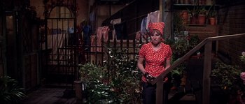 Movie still from “On a Clear Day You Can See Forever” (1970), directed by Vincente Minnelli – A woman in a red polka dot shirt standing in front of a fence; Medium shot, High angle