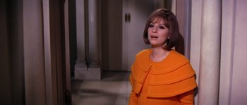 Movie still from “On a Clear Day You Can See Forever” (1970), directed by Vincente Minnelli – A woman in an orange dress standing in front of a doorway; Medium shot, Over the shoulder angle