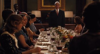 Movie still from “On the Basis of Sex” (2018), directed by Mimi Leder – A man standing in front of a long table of food; Medium shot, Over the shoulder angle