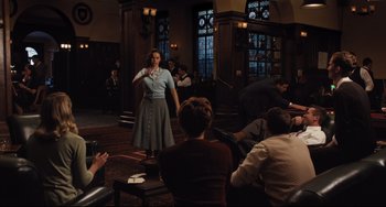 Movie still from “On the Basis of Sex” (2018), directed by Mimi Leder – A woman standing in front of a group of people in a room; Wide shot, Over the shoulder angle