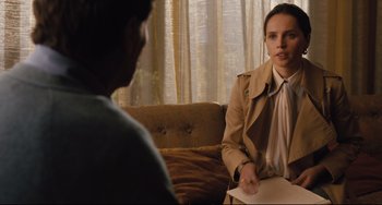 Movie still from “On the Basis of Sex” (2018), directed by Mimi Leder – A woman in a trench coat talking to a man in front of a couch; Medium shot, Over the shoulder angle