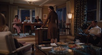Movie still from “On the Basis of Sex” (2018), directed by Mimi Leder – A woman standing in front of a group of people in a living room; Wide shot, Over the shoulder angle