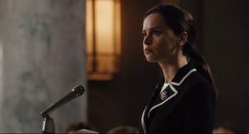 Movie still from “On the Basis of Sex” (2018), directed by Mimi Leder – A woman standing in front of a microphone in a room; Close Up shot, Over the shoulder angle