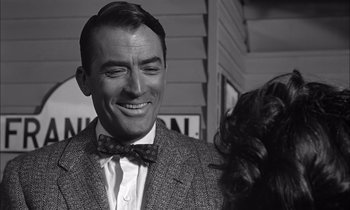 Movie still from “On the Beach” (1959), directed by Stanley Kramer – A black and white photo of a man in a suit and a bow tie; Close Up shot, Over the shoulder angle