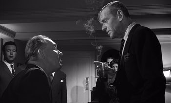 Movie still from “On the Beach” (1959), directed by Stanley Kramer – A man smoking a cigarette while another man looks at him; Medium shot, Over the shoulder angle