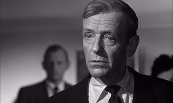 Movie still from “On the Beach” (1959), directed by Stanley Kramer – A black and white photo of a man in a suit and tie; Close Up shot, Over the shoulder angle