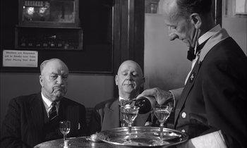 Movie still from “On the Beach” (1959), directed by Stanley Kramer – A man pouring a drink into a wine glass at a table; Medium shot, Low angle